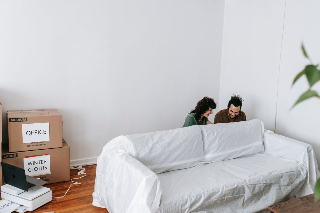 A couple is enjoying their move into a new home, with boxes around them and minimalist decor.